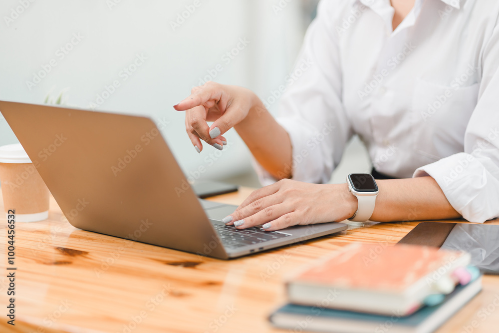 person is working on laptop, engaged in task while sitting at wooden table. scene conveys productive atmosphere, with coffee cup and books nearby, suggesting workspace. person is working on laptop, engaged in task while sitting at wooden table. scene conveys productive atmosphere, with coffee cup and books nearby, suggesting workspace.