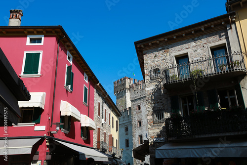 Colorful Street with Sirmione Castle Tower in the Background A vibrant street in Sirmione, Italy, featuring colorful buildings and the medieval tower of Sirmione Castle peeking from behind.