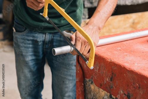 Close up of a person's hands cutting a pipe with a yellow saw blade