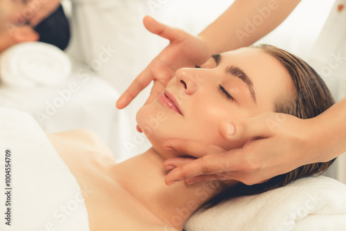 Caucasian couple enjoying relaxing anti-stress head massage and pampering facial beauty skin recreation leisure in dayspa modern light ambient at luxury resort or hotel spa salon. Quiescent