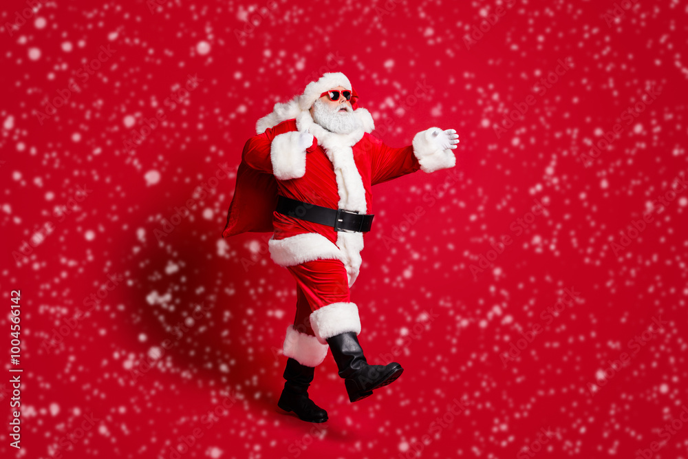Full length profile photo of retired old man grey beard walk bear bag gift responsible grandpa hurry before midnight wear santa costume sunglass headwear boots isolated red color background Full length profile photo of retired old man grey beard walk bear bag gift responsible grandpa hurry before midnight wear santa costume sunglass headwear boots isolated red color background