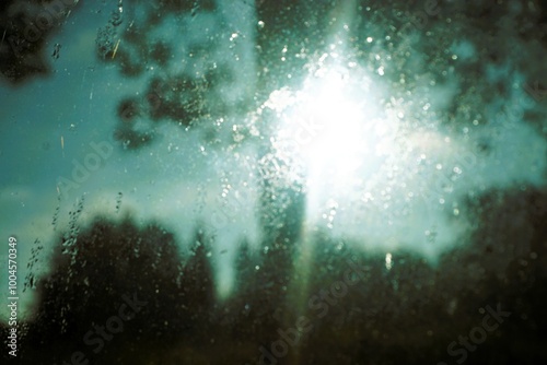 Abstraktes Motiv mit beschlagener Glasscheibe vor grünem Baum, Wald, Himmel und weißem Sonne bei Nebel, Frost und Sonne am Morgen im Herbst photo