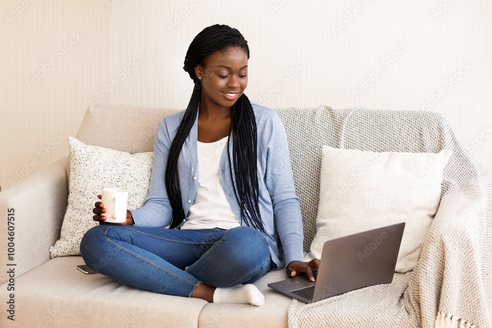 Working From Home Concept. Black Millennial Girl Using Laptop At Home For Freelance Work, Sitting On Sofa And Drinking Coffee, Copy Space Working From Home Concept. Black Millennial Girl Using Laptop At Home For Freelance Work, Sitting On Sofa And Drinking Coffee, Copy Space