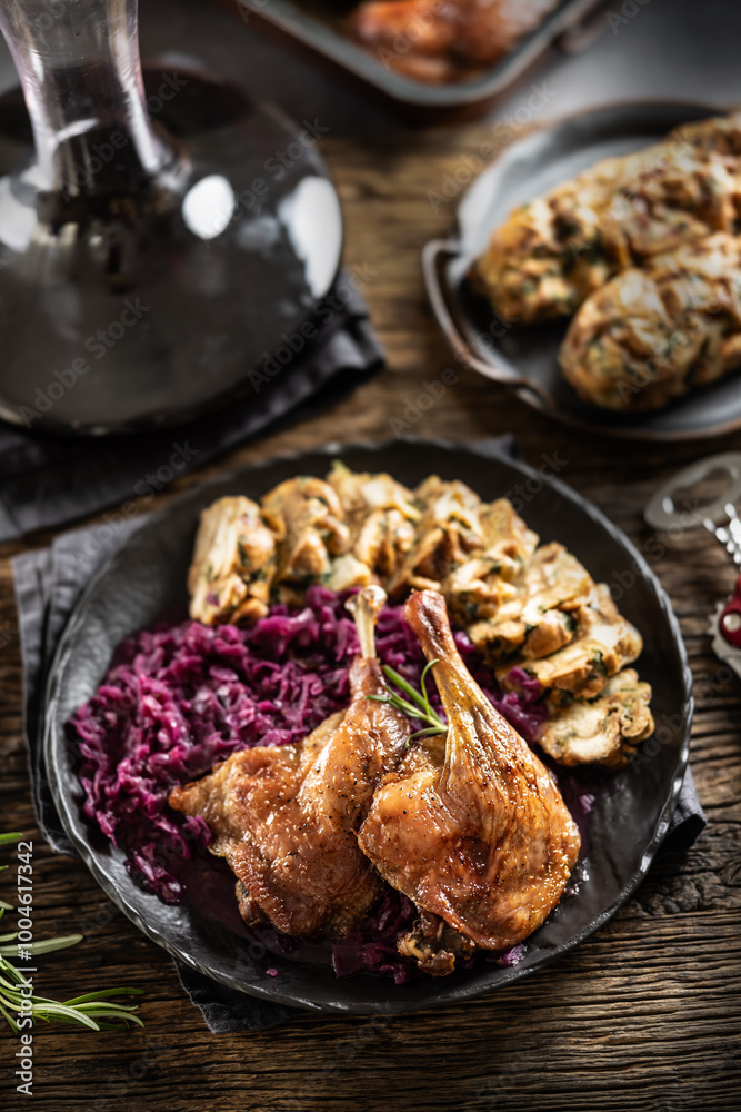 Fototapeta premium Portion of roast duck leg red cabbage homemade dumplings on plate and red wine on the background