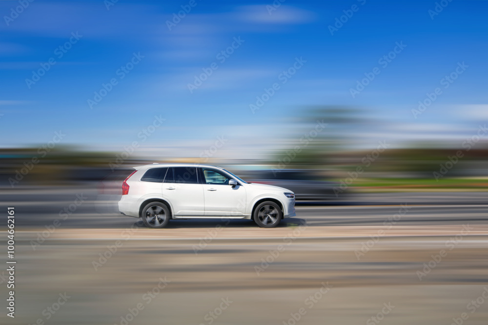 Fototapeta premium Fast moving car. A white SUV is driving on the highway at high speed on a blurred background