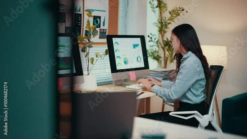 Asian businesswoman sits at her desk, working on a computer. Analyzing data and managing spreadsheets, she demonstrates professionalism in a corporate environment