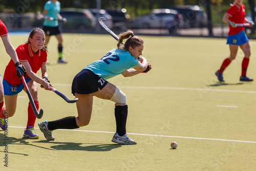 Female attacker hitting the ball in an intense field hockey match on a sunny afternoon photo