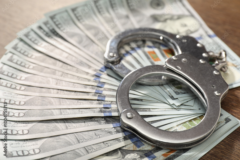 Handcuffs with dollar banknotes on table, closeup Handcuffs with dollar banknotes on table, closeup