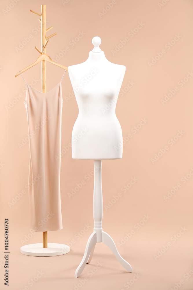 One female mannequin on stand and rack with dress against beige background One female mannequin on stand and rack with dress against beige background