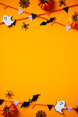 Halloween composition with cute bats, ghosts, pumpkins, spiders, bunting flag garland on orange background. Happy Halloween vertical banner mockup, poster design. Flat lay, top view, copy space.