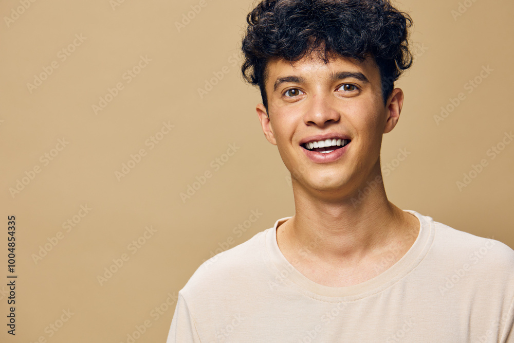 Happy young man smiling with curly hair in a light beige shirt against a warm beige background, representing joy and positivity in a casual setting Happy young man smiling with curly hair in a light beige shirt against a warm beige background, representing joy and positivity in a casual setting
