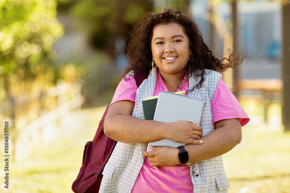 A cheerful student smiles while holding several books close to her chest. She walks along a pathway on campus, enjoying a sunny afternoon with greenery around her. A cheerful student smiles while holding several books close to her chest. She walks along a pathway on campus, enjoying a sunny afternoon with greenery around her.