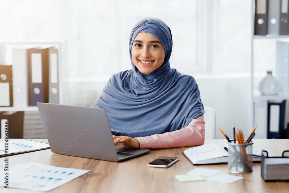 Modern Job For Muslim Women. Portrait of happy islamic girl in hijab working on laptop in office and looking at camera, copy space Modern Job For Muslim Women. Portrait of happy islamic girl in hijab working on laptop in office and looking at camera, copy space