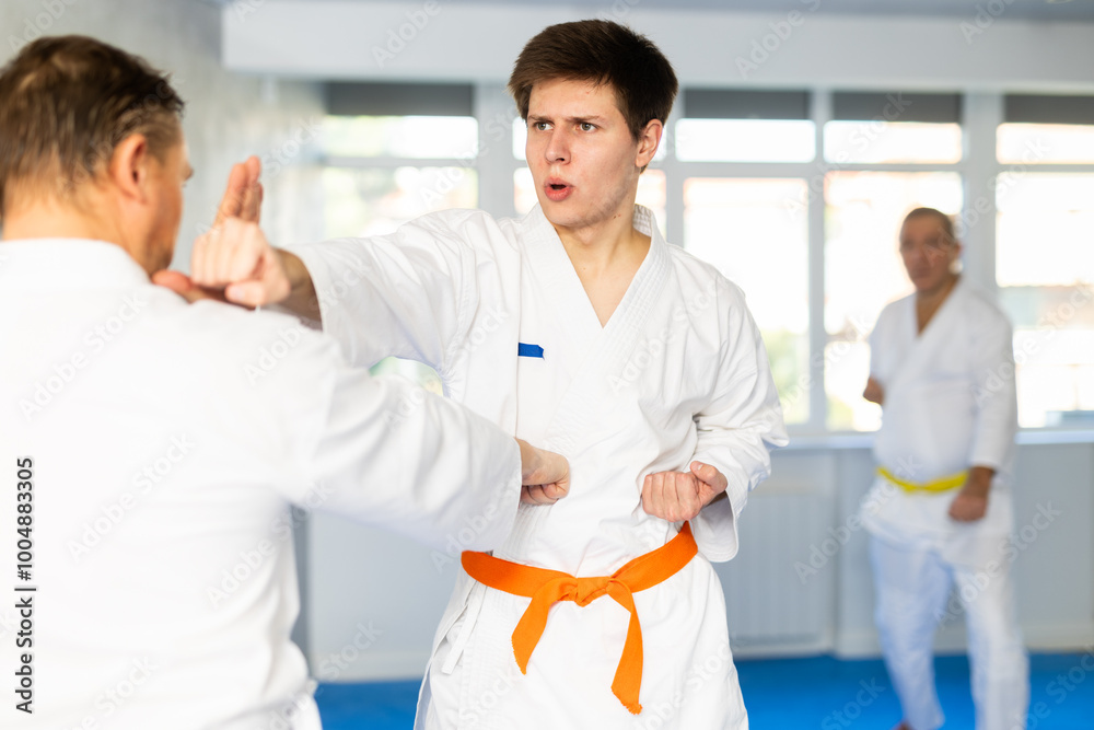 Obraz premium Adult man and young guy in kimono train karate fight in studio