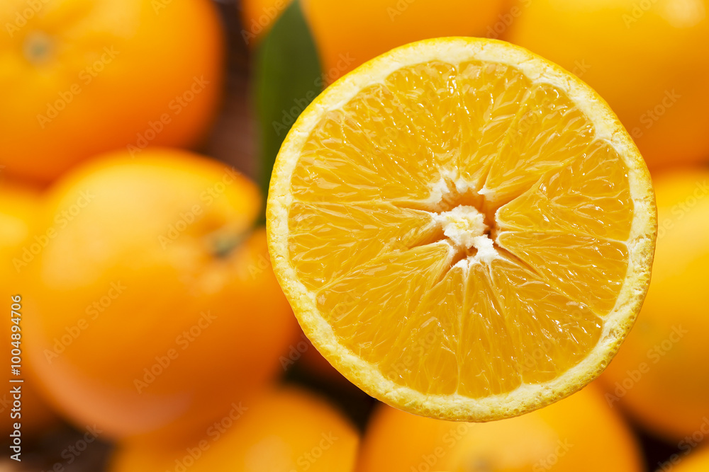 Fototapeta premium A juicy orange slice, bursting with sunshine, sits against a backdrop of whole oranges, creating a vibrant display of color.