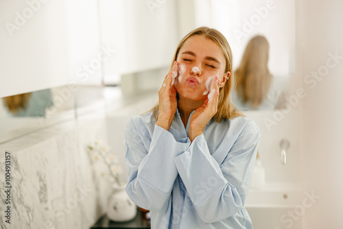 A young woman joyfully applies her favorite facial cleanser, enjoying her skincare routine in a bright, serene bathroom