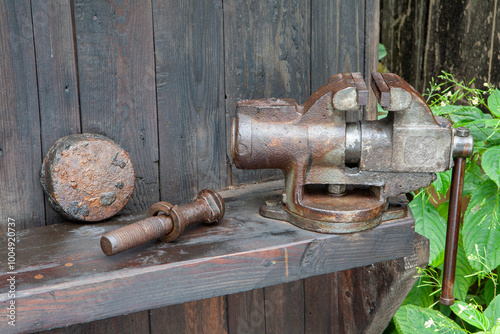 Grandpa's old rusty vice attached to a wooden shelf on the outside wall of a weathered barn