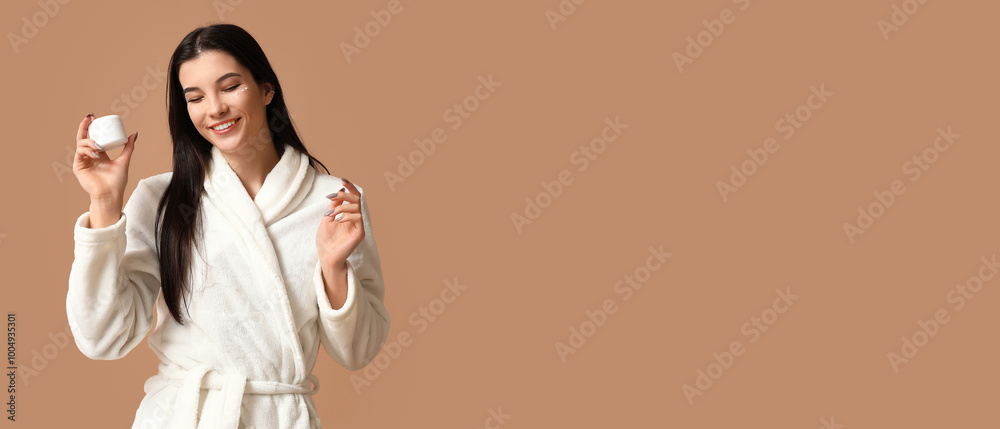 Beautiful young woman in bathrobe holding jar of cream on beige background with space for text Beautiful young woman in bathrobe holding jar of cream on beige background with space for text