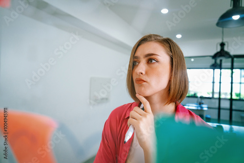 Portrait of young caucasian businesswoman thinking with confused face expression while standing in front of glass board with sticky notes and mind map at creative business meeting. Immaculate.