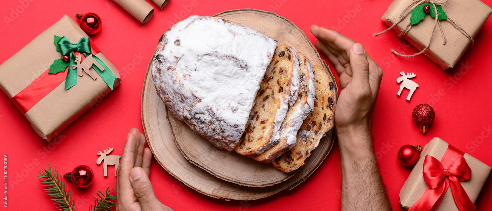 Male hands with tasty Christmas stollen and decor on red background Male hands with tasty Christmas stollen and decor on red background