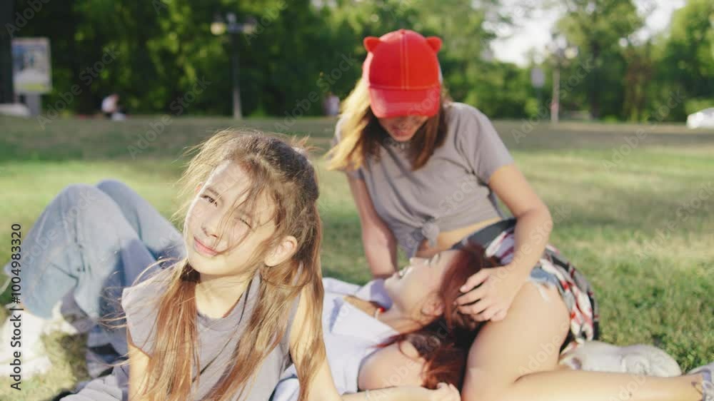 A beautiful portrait of the daughter looking at the camera, while her two mothers lie on a blanket in the background, tenderly stroking each other. The scene captures a loving family moment.