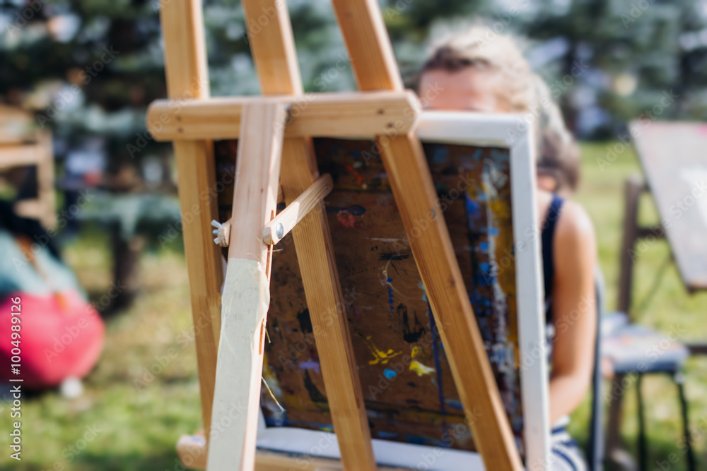 Kids drawing at plein air, group class of talented children with painting easel and wooden canvas during lesson of watercolor painting outdoors, drawing class for young teen artists in art school Kids drawing at plein air, group class of talented children with painting easel and wooden canvas during lesson of watercolor painting outdoors, drawing class for young teen artists in art school