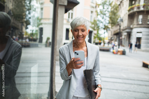 Senior businesswoman walking in city using smartphone photo