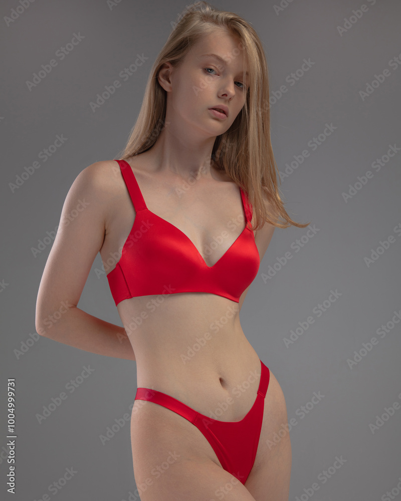 Naklejka premium A model showcases a striking red lingerie set, embodying elegance and poise. The neutral background emphasizes her confident stance and the garment's design.