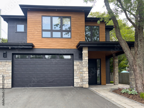 Fototapeta Naklejka Na Ścianę i Meble -  A street view of a modern suburban-style house. There's a patio, the exterior walls are faux wood siding and beige rock, and the garage door is a large brown metal door with small glass windows.   
