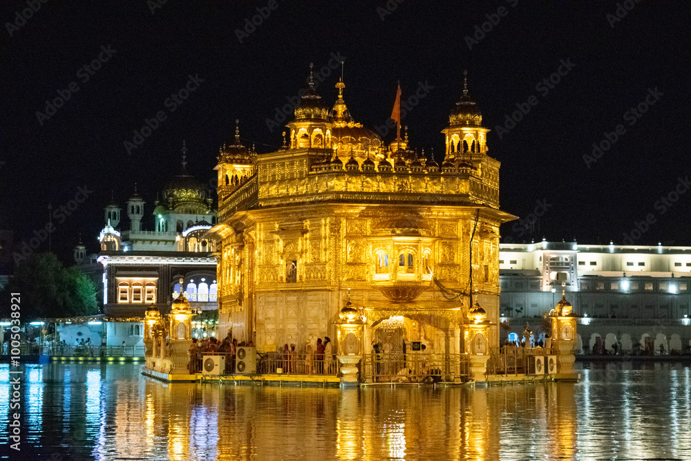 Fototapeta premium The golden temple of amritsar glowing at night with pilgrims reflecting in the water