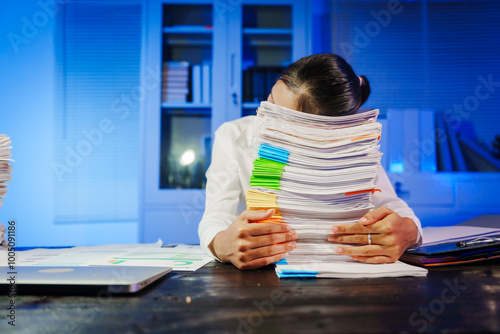 confident Asian businesswoman works late into the night, surrounded by a stack of papers in a busy office. Overtime leads to office syndrome symptoms like neck pain, headaches, and chronic stress. photo