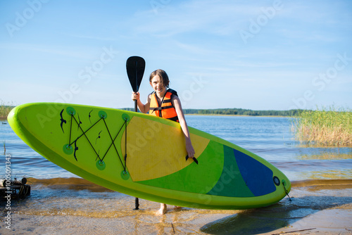 boy carries stand up paddle board from lake to shore after riding