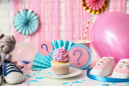 Delicious cupcake with question marks, baby booties and decorations on table against white brick background. Gender reveal party concept photo