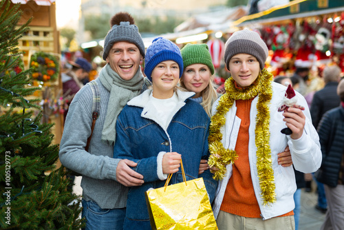 Portrait of cheerful man and woman and their happy teenagers posing with paper bags near counters at Christmas fair photo