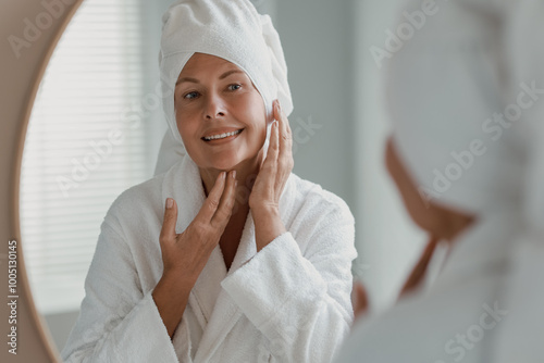 Beautiful woman doing facial massage near mirror at home