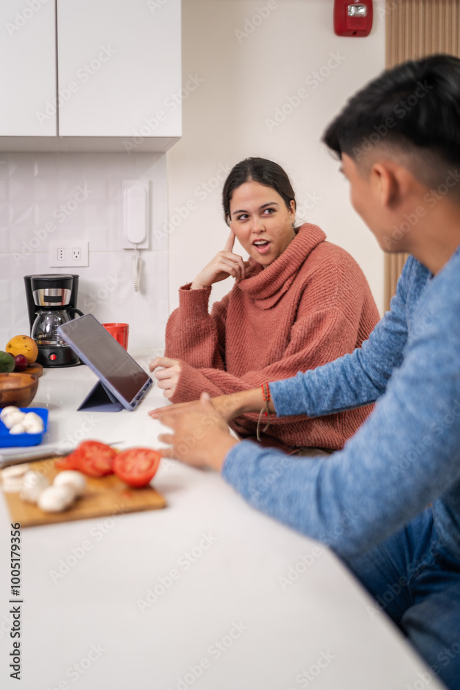 Young couple cooking together following recipe on tablet in kitchen Young couple cooking together following recipe on tablet in kitchen