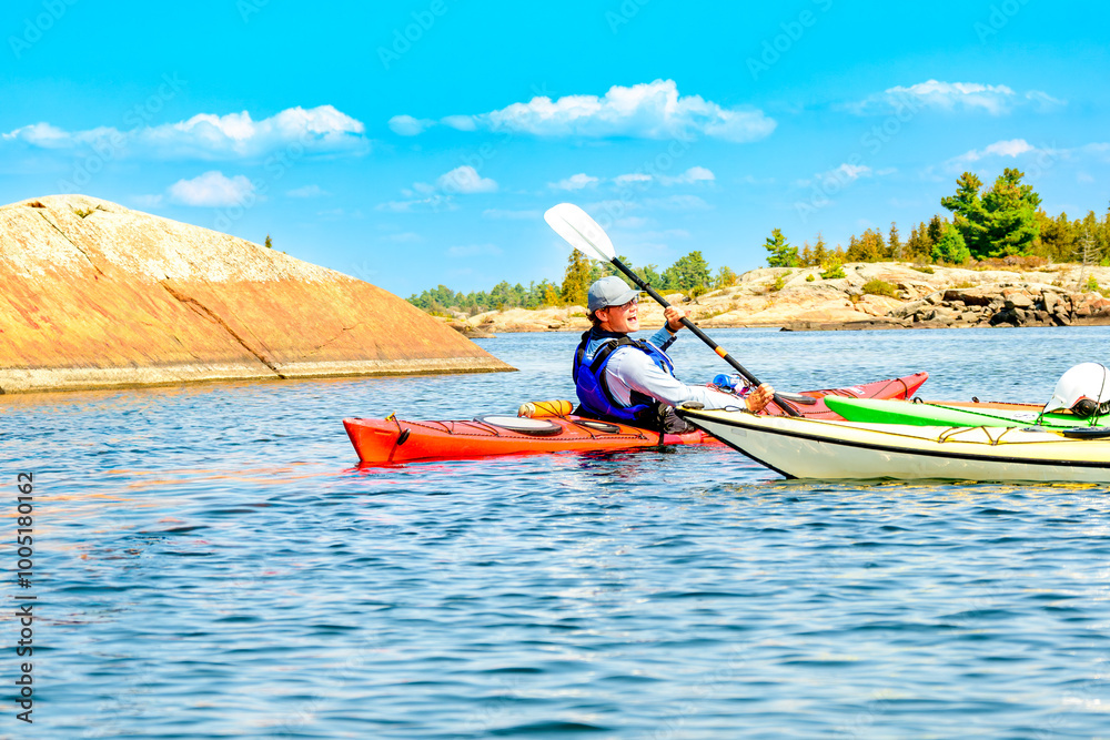 Naklejka premium young man paddling on a multiday sea kayak expedition on georgian bay ontario room for text
