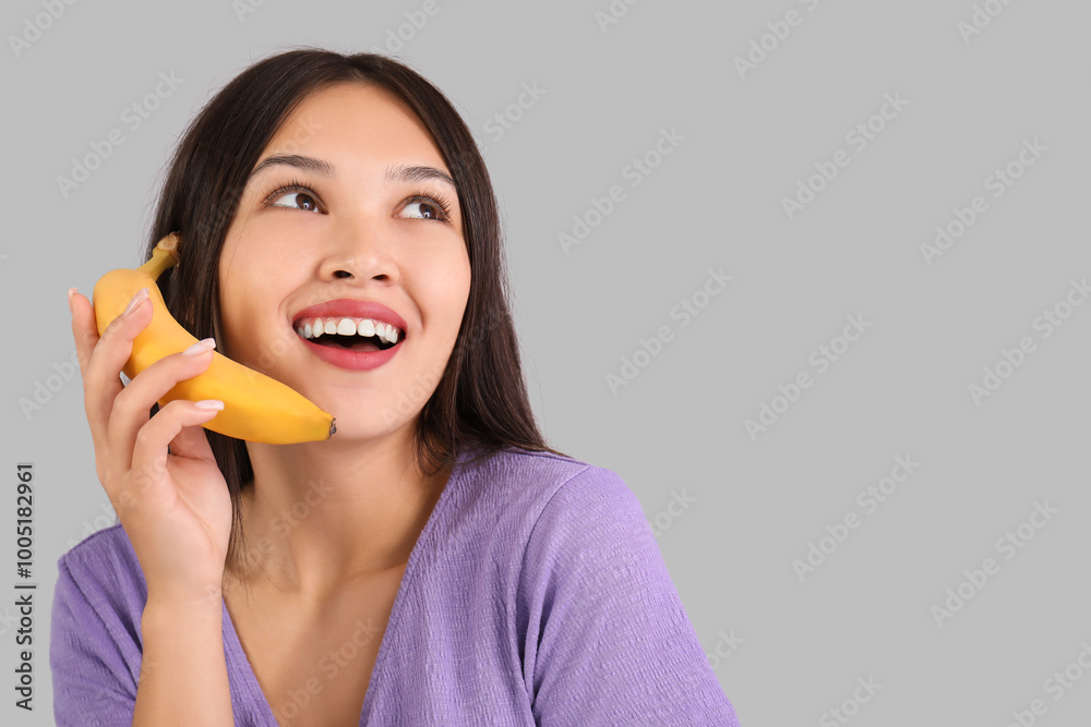 Beautiful young Asian woman with fresh banana on grey background Beautiful young Asian woman with fresh banana on grey background
