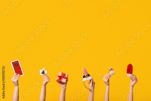 Female hands with gift box, elf hat headband and different Christmas decorations on yellow background