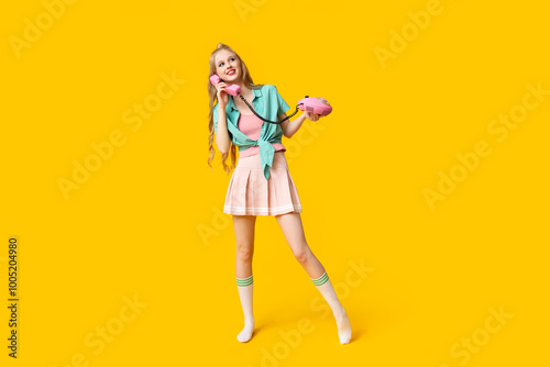 Beautiful young happy woman with retro telephone on yellow background