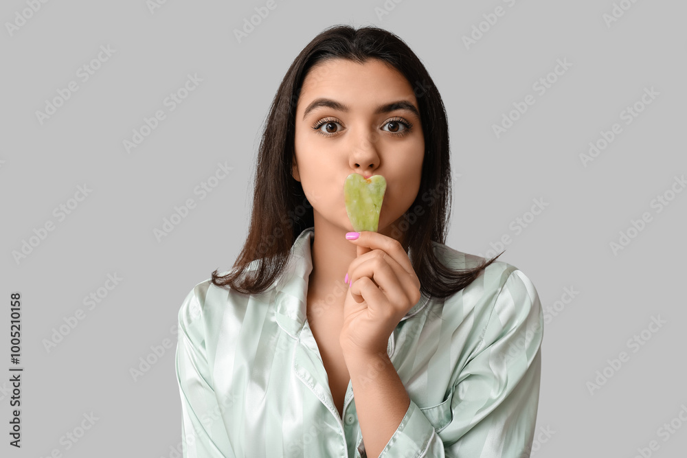 Beautiful young woman with guasha facial tool on grey background Beautiful young woman with guasha facial tool on grey background