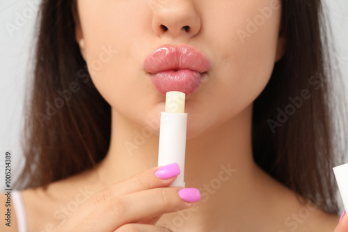 Young woman applying lip balm on grey background, closeup