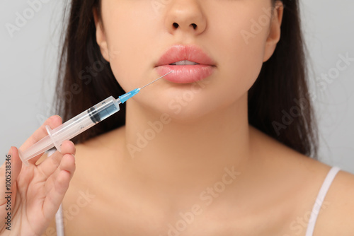 Beautiful young woman receiving lip injection on grey background, closeup