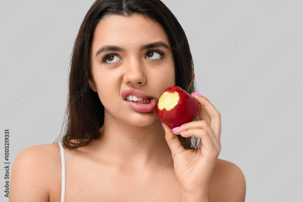 Emotional young woman with bitten apple on grey background Emotional young woman with bitten apple on grey background