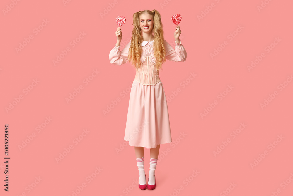 Beautiful young happy woman dressed as doll with heart-shaped lollipops on pink background. Valentine's Day celebration Beautiful young happy woman dressed as doll with heart-shaped lollipops on pink background. Valentine's Day celebration