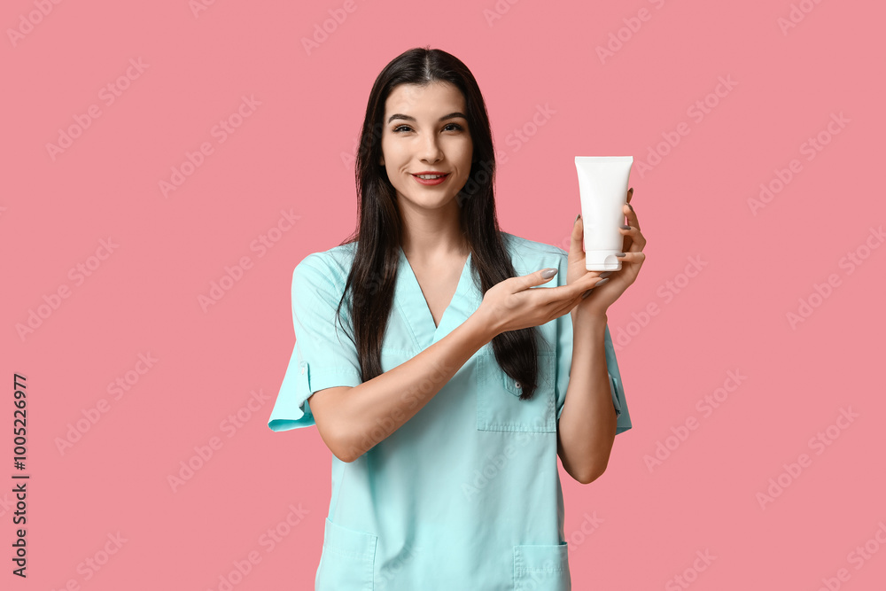 Beautiful young female beautician with bottle of cosmetic product on pink background Beautiful young female beautician with bottle of cosmetic product on pink background