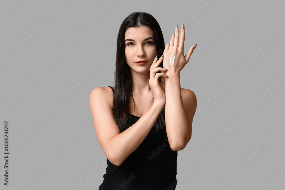 Beautiful young woman with cream on her arm against grey background Beautiful young woman with cream on her arm against grey background