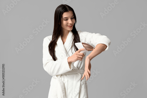 Beautiful young happy woman in bathrobe with modern photoepilator on grey background photo