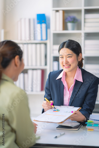 Two successful Asian businesswomen working with financial data graph documents and laptops in business data analysis.