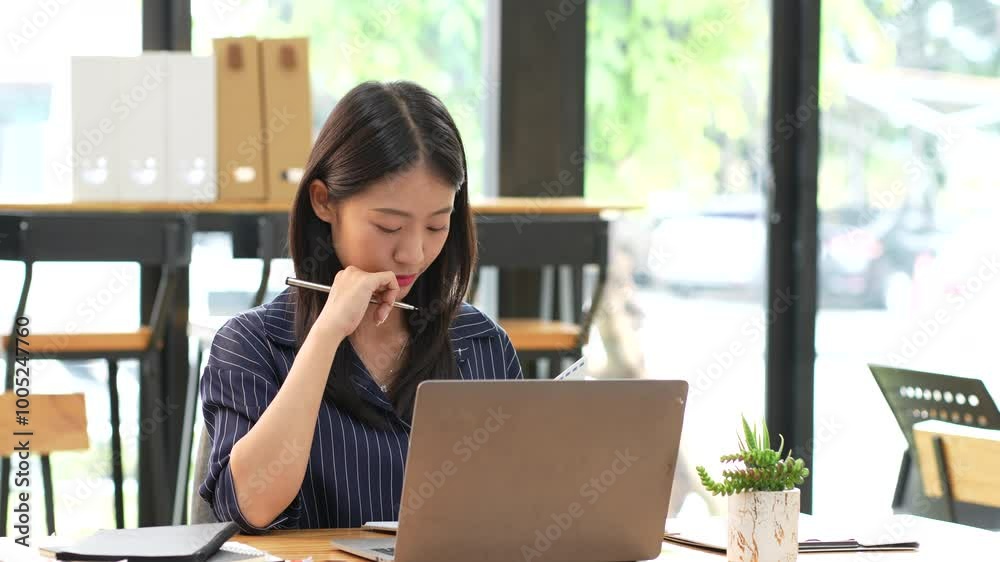 Focused woman working on laptop in modern office setting, deep in thought while holding pen. atmosphere is calm and productive, ideal for concentration and creativity. Focused woman working on laptop in modern office setting, deep in thought while holding pen. atmosphere is calm and productive, ideal for concentration and creativity.